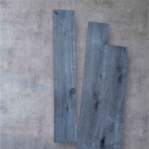 Three rustic grey LVT tiles leaning against a textured grey wall.